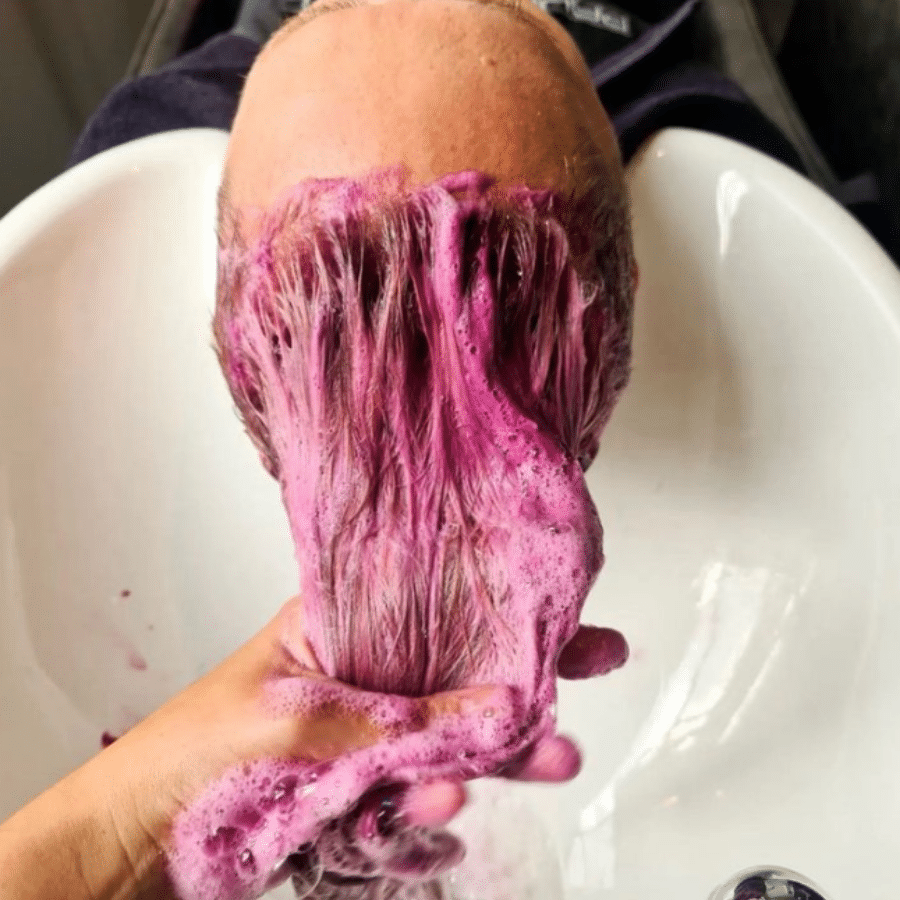 woman with hair at a basin with ultra rose shampoo being applied. the suds are very pink and striking