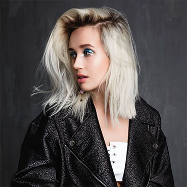 Bright platinum blonde with head turned to the side, long bob, wearing black bomber style jacket