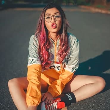 Lady with bright pink long hair wearing red converse shoes, vans socks and long sleeve active wear jacket sitting in the middle of a country road