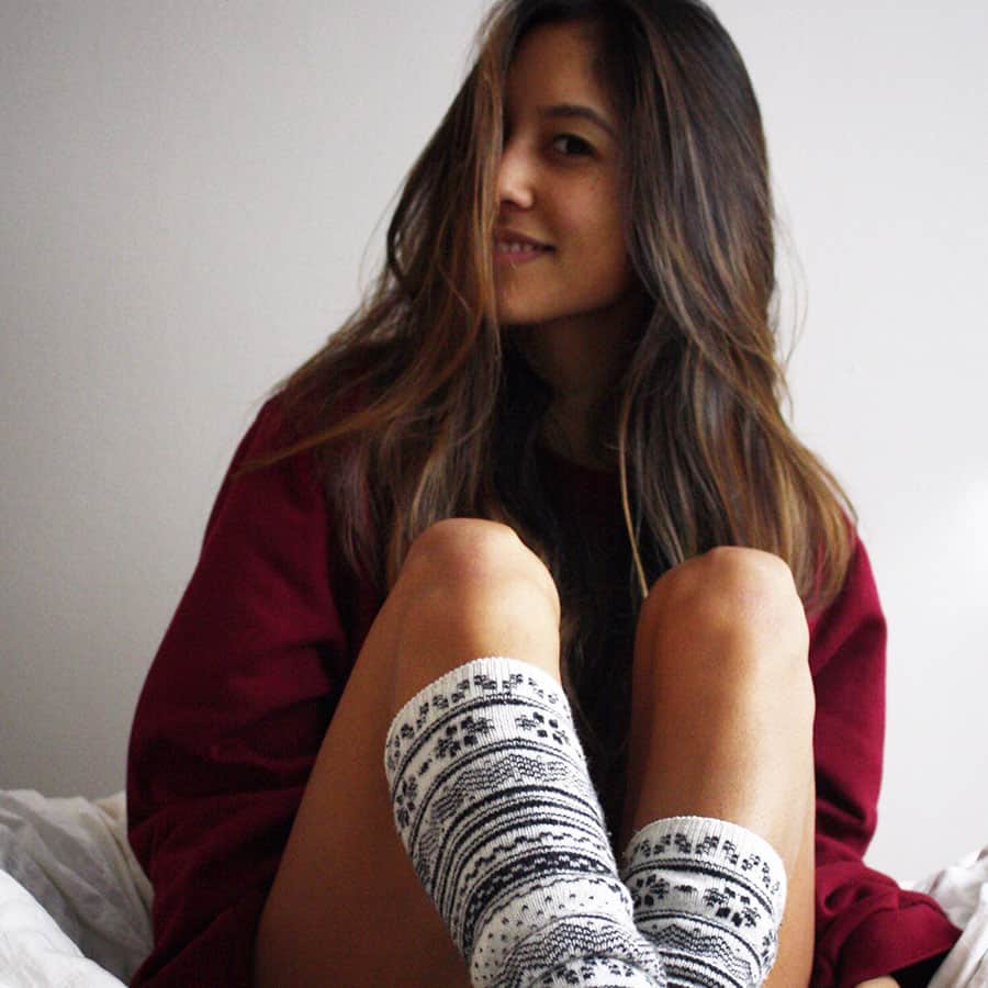 long brunette haired lady sitting on a bed in comfy red sweater and long black and white socks