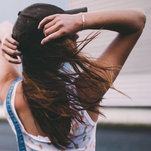 Brunette met door de wind geblazen haar draagt een baseballpet met haar rug naar de camera