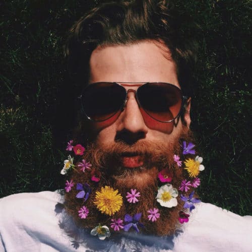 man with many colourful flowers in his ginger beard, wearing dark aviator glasses
