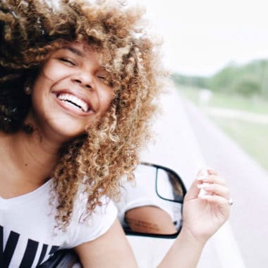 lady with head out of car window and very tight curly hair being blown in the breeze