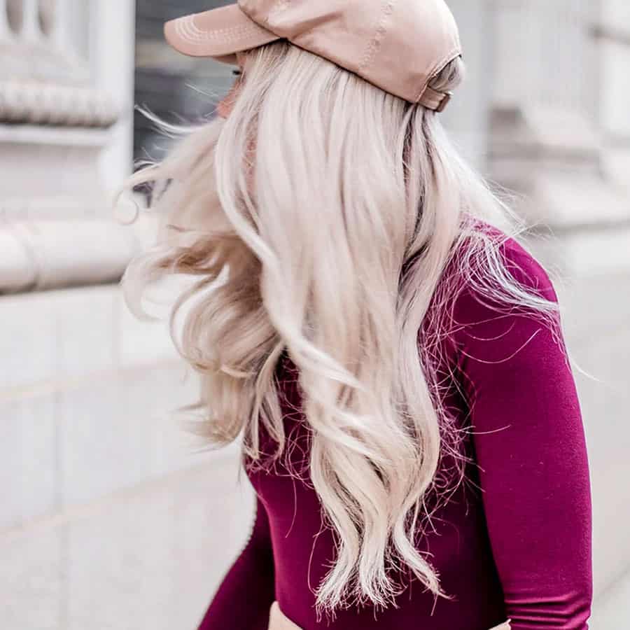 Side profile of girl with long clean blonde hairweaving pale pink cap and long sleeve cherry pink top walking in city streetscape