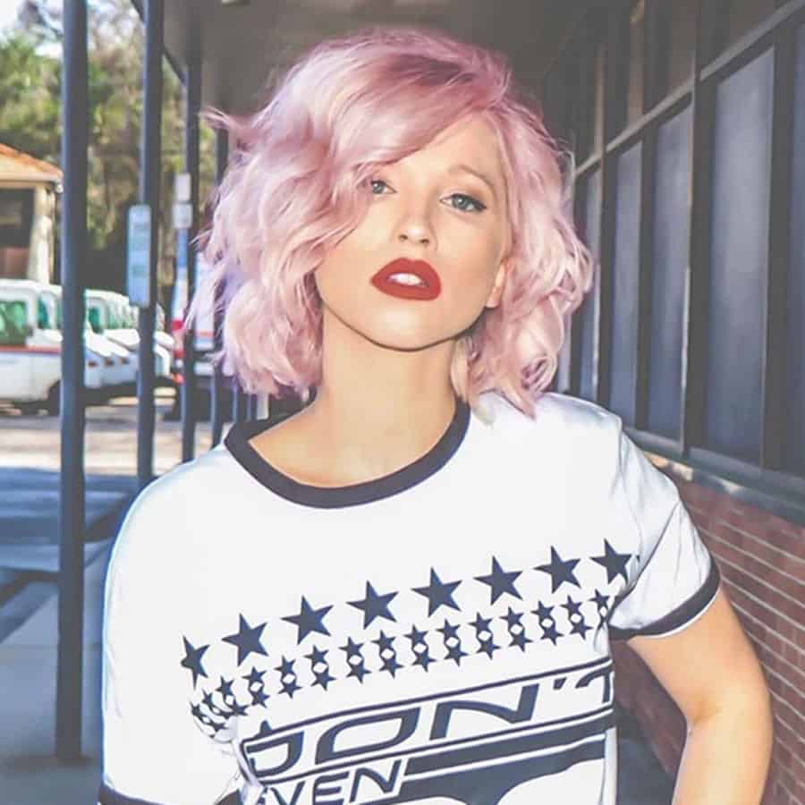 very vibrant pink textured bob hair on a lady with bright red lipstick wearing a white shirt standing in a streetscape with parked vans in the background