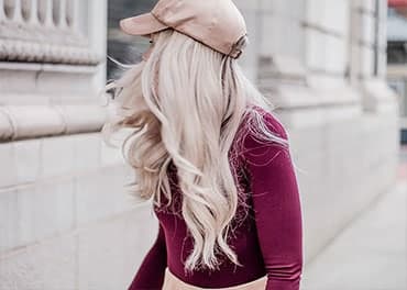 Side profile of girl with long clean blonde hairweaving pale pink cap and long sleeve cherry pink top walking in city streetscape
