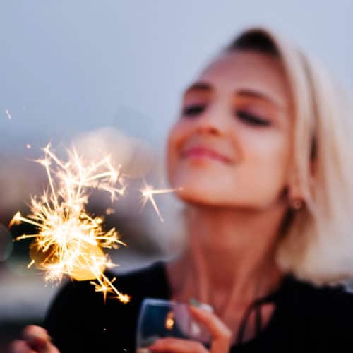 Blonde lady with a glittering sparkler holding a glass of wine