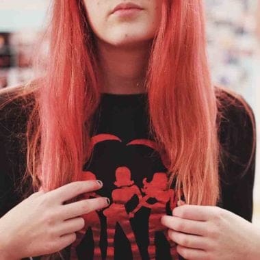 Female with black printed t shirt, showing bottom half of face. Hands holding ends of long peach coloured hair