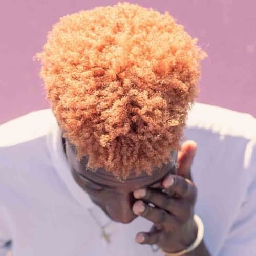 Top view of man's head with tight curly peach hair. Man holding left hand over left eye.
