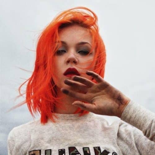 model with bright, neon red, orange, shoulder length hair looking at camera