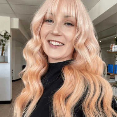 Girl with long curly hair and fringe. Colour of her hair is a very light, pastel peach colour.