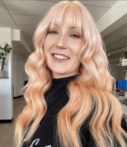 Girl with long curly hair and fringe. Colour of her hair is a very light, pastel peach colour.
