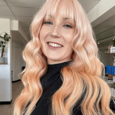 Girl with long curly hair and fringe. Colour of her hair is a very light, pastel peach colour.