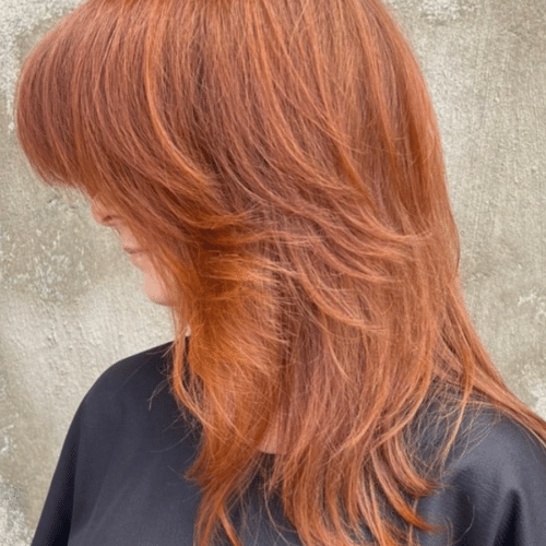woman with red hair cut into a wolf cut looking to the side